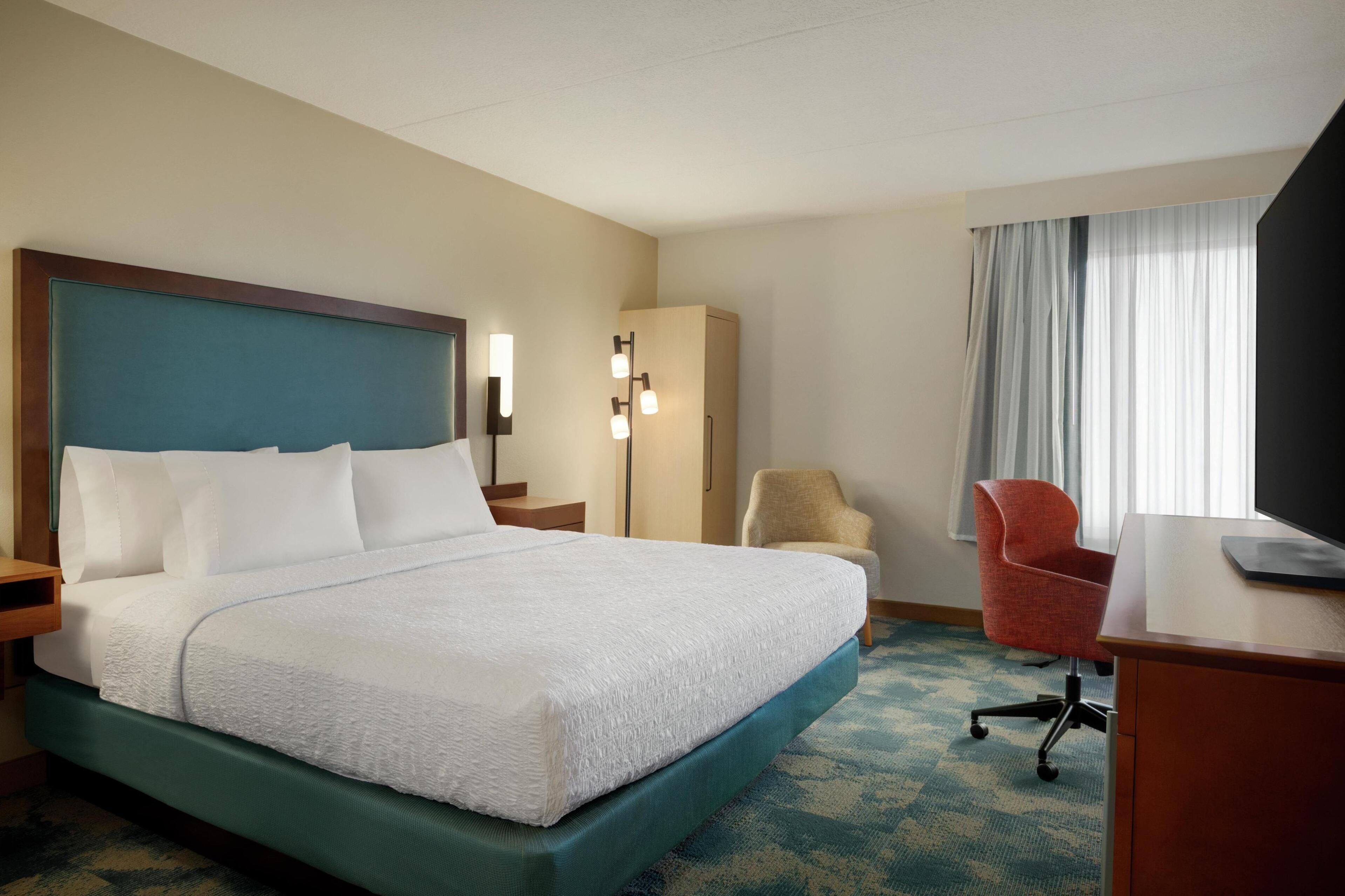 A hotel room with a large bed, a desk, a chair, and a wardrobe.