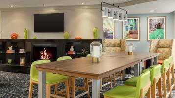 A dining area with a long wooden table, green upholstered chairs, a fireplace, and framed artwork on the walls.