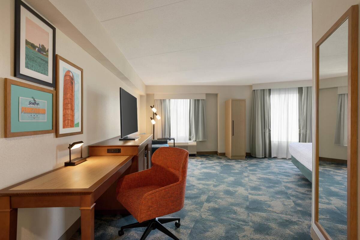 A hotel room with a desk, chair, TV, and a bed.
