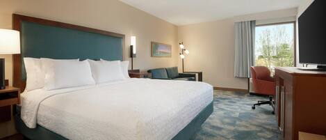 A hotel room with a large bed, a desk, a chair, a TV, and a window with a view.