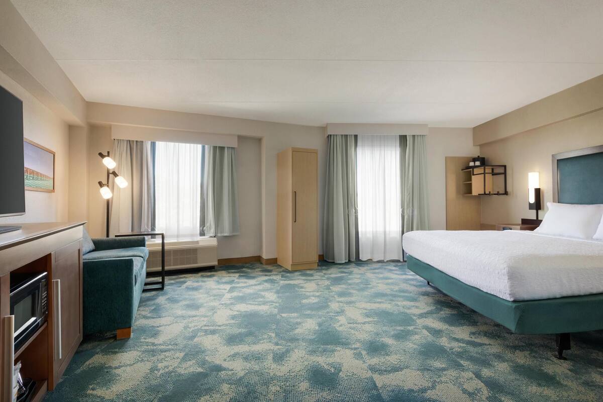A hotel room with a bed, a desk with a computer, a sofa, and a TV.