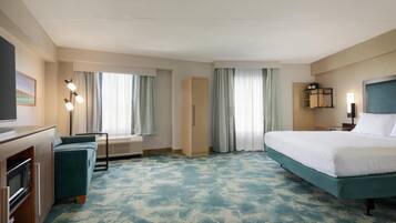 Et hotelværelse med seng, skrivebord med computer, sofa og fjernsyn.