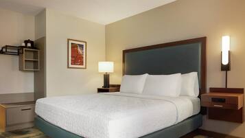 A hotel room with a large bed, a bedside table with a lamp, a small shelf, and a framed picture on the wall.