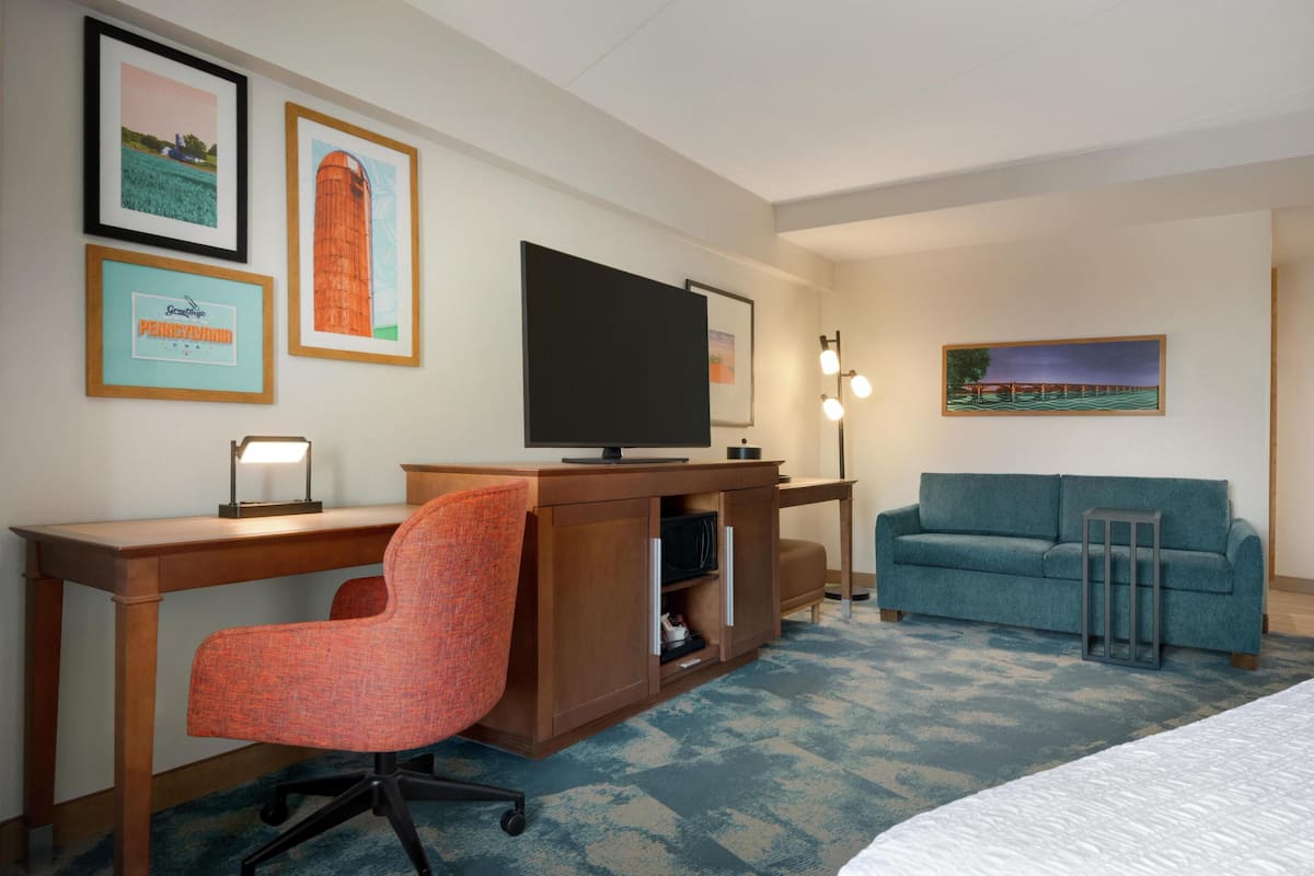 A hotel room with a wooden desk, a television, a blue sofa, and framed pictures on the wall.