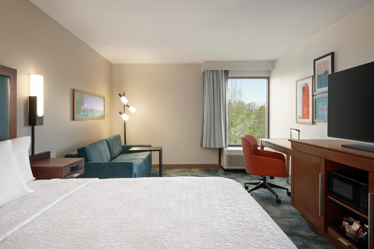 A hotel room with a large bed, a desk with a chair, a television, and a window with curtains.