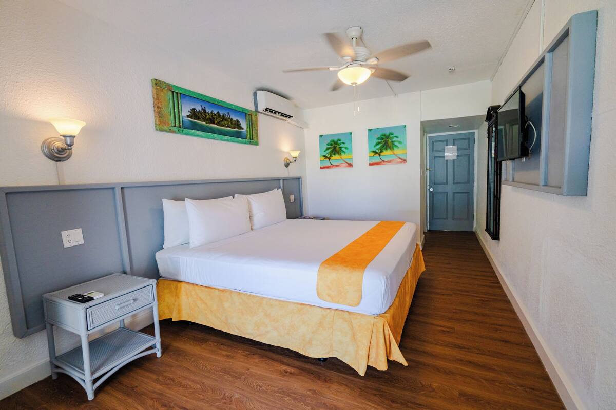 A neatly made bed with a white and orange bedspread, a small bedside table with a lamp, and a ceiling fan.