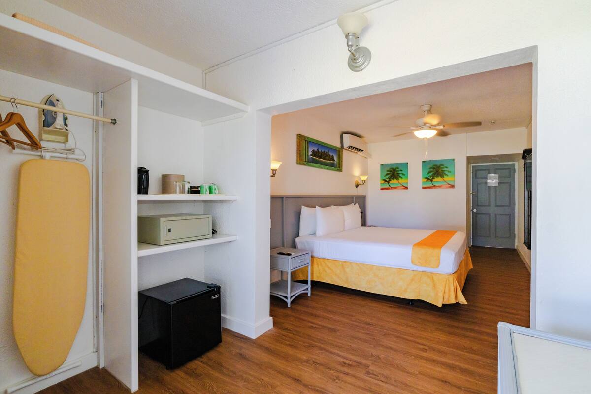 A room with a bed, a shelf with items, a small table, and a door.