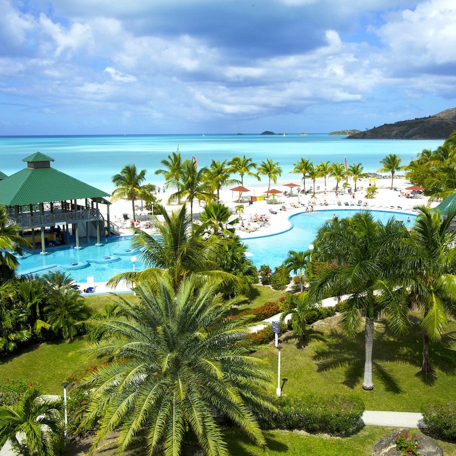 A resort with a pool, palm trees, and a view of the ocean.