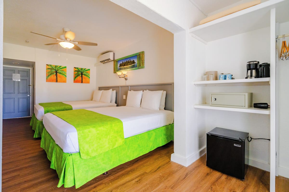 A hotel room with two beds, a ceiling fan, a small refrigerator, and a shelf with a coffee maker.