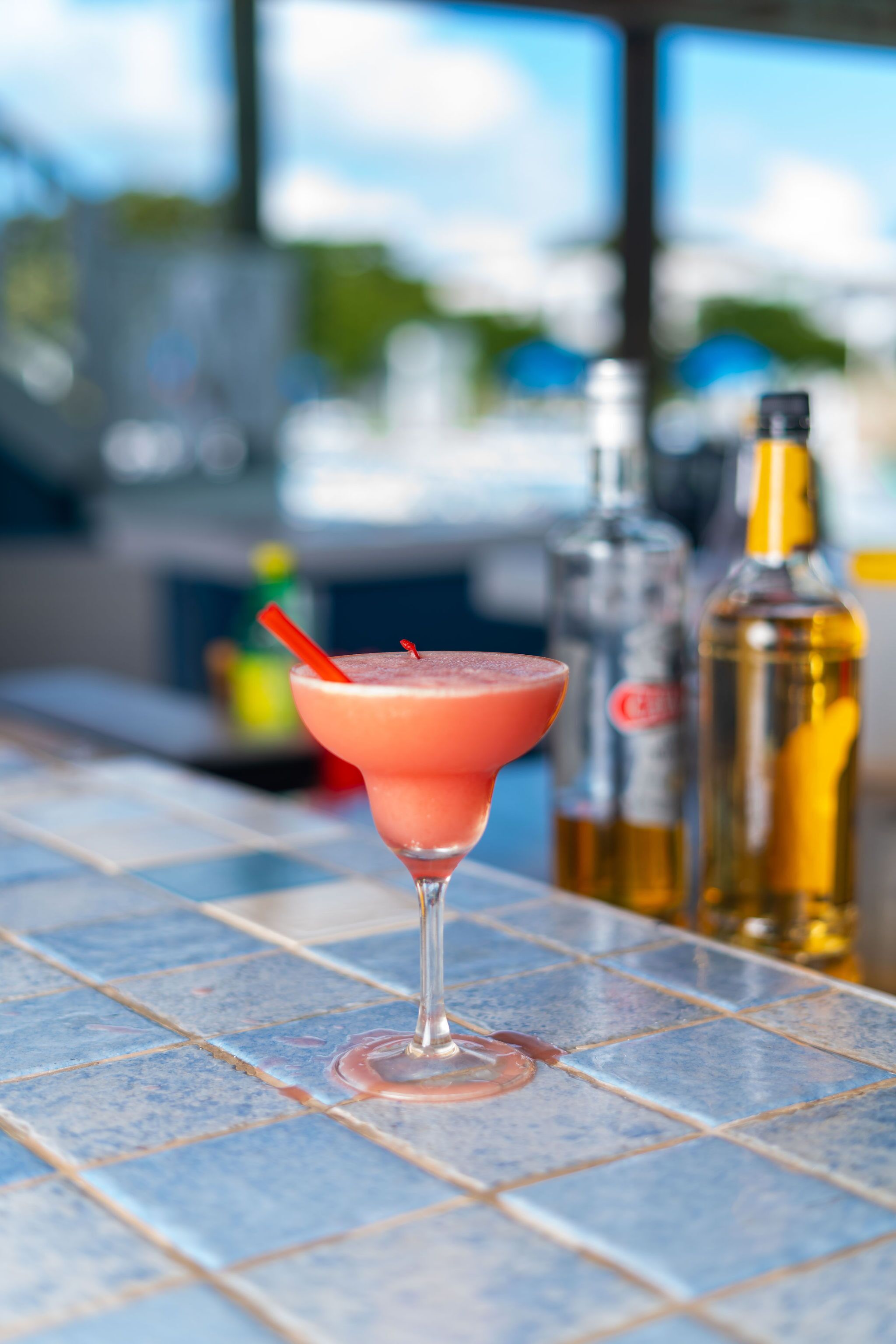A cocktail in a glass with a red straw on a tiled bar counter.