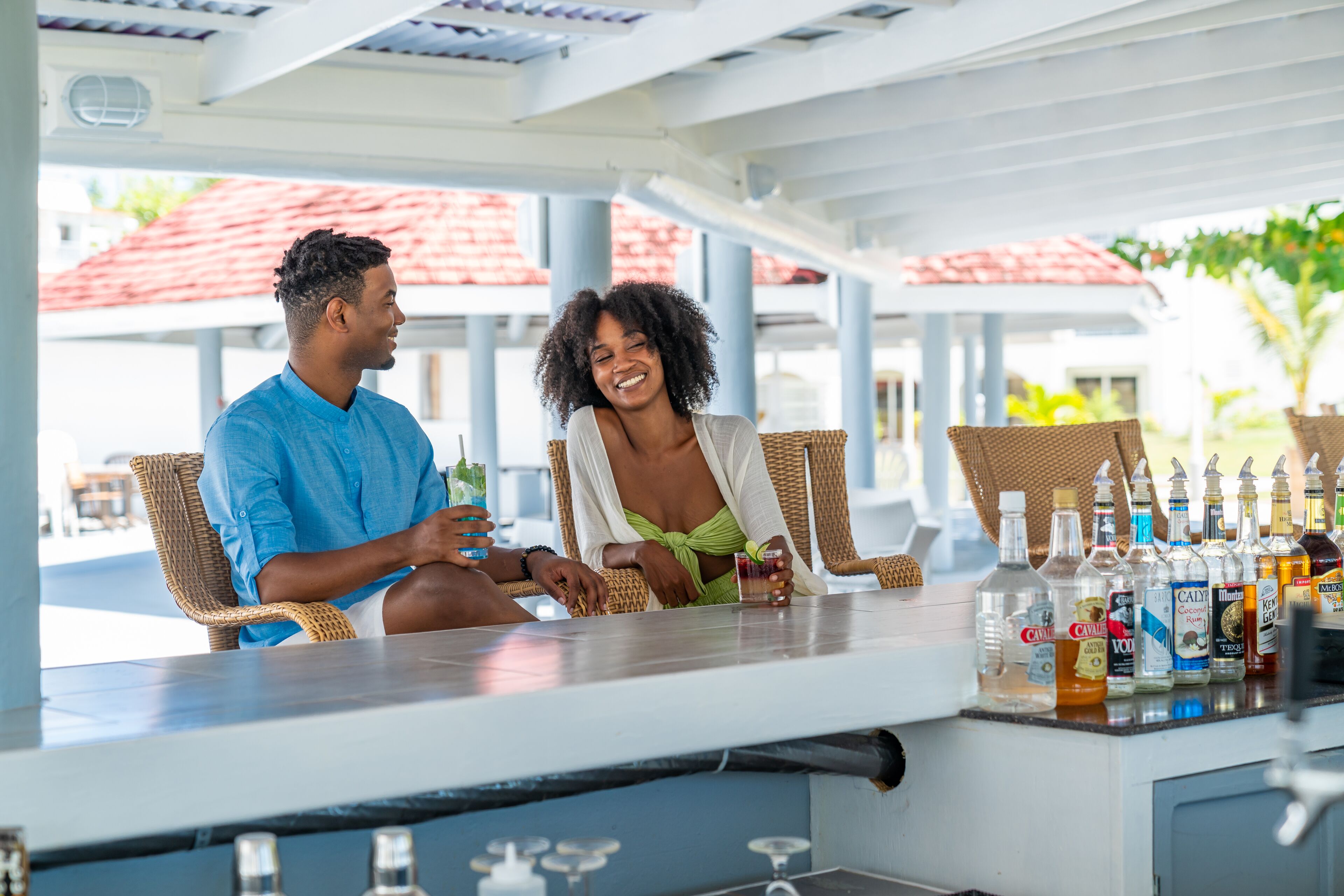 A couple seated at a bar with a variety of bottles and glasses.
