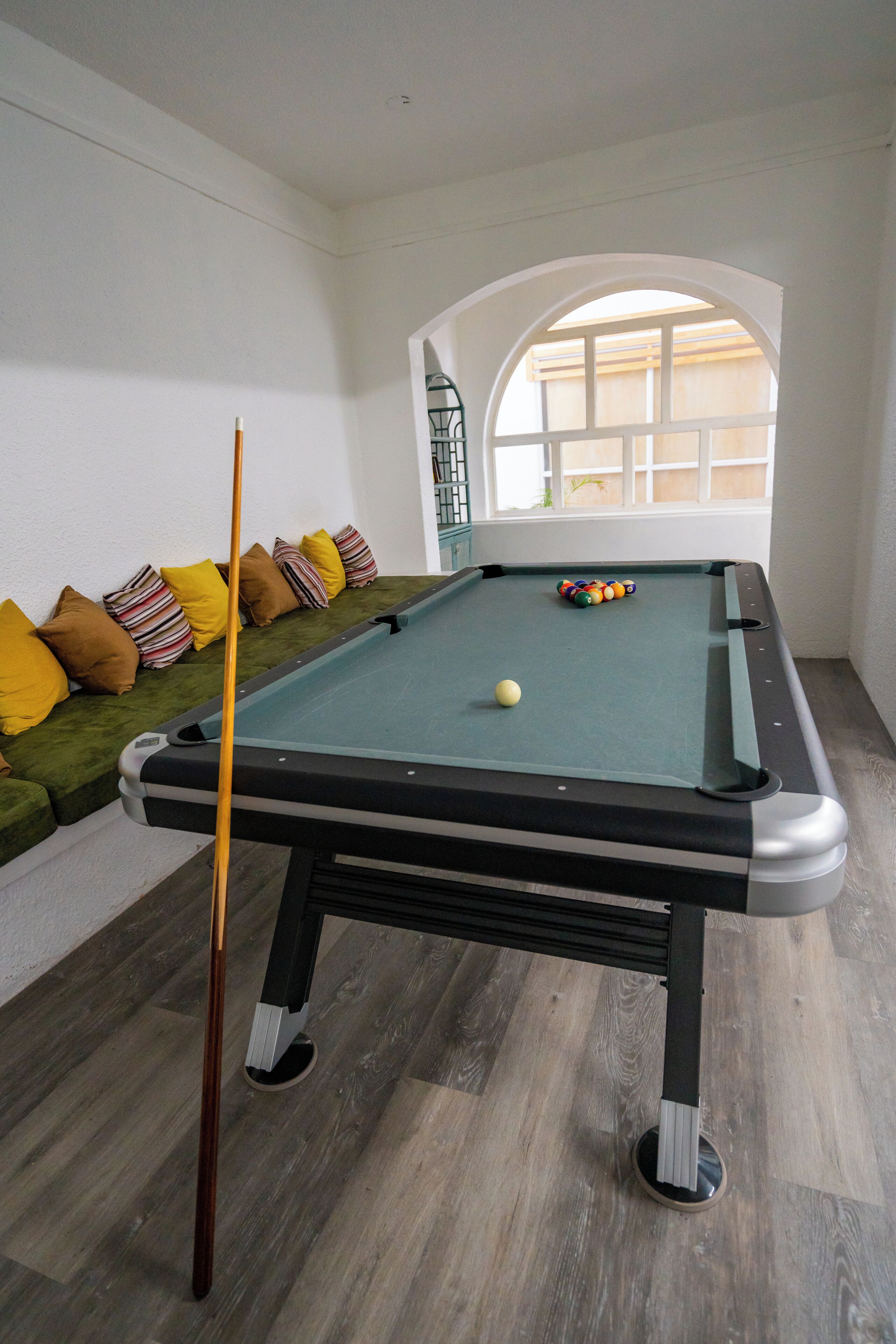 Une table de billard avec une seule boule, une queue de billard et un canapé avec des coussins.