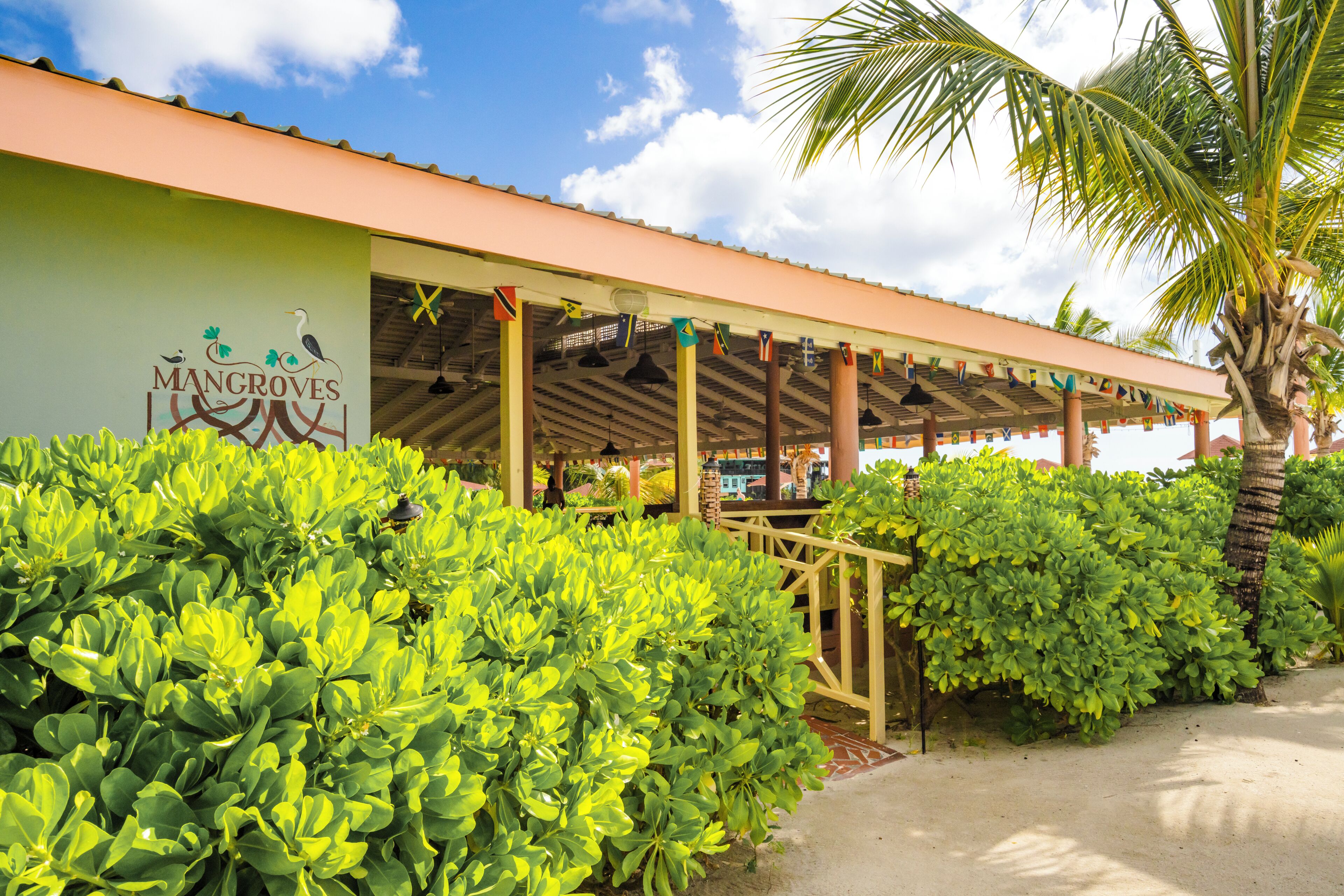 A building with a sign reading 'Mangroves' and a covered outdoor area with plants and a palm tree.
