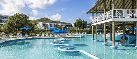 Une piscine entourée de bâtiments et de palmiers, avec des chaises longues et des parasols.