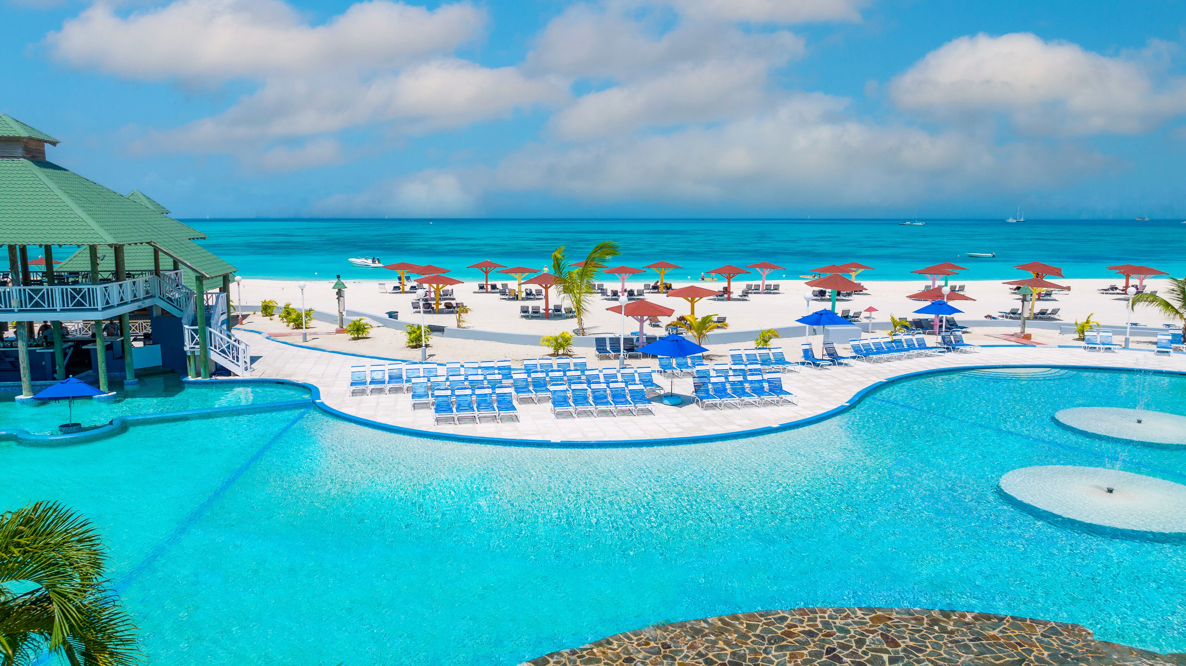 A resort pool area with lounge chairs and umbrellas, a pool, and a view of the ocean.