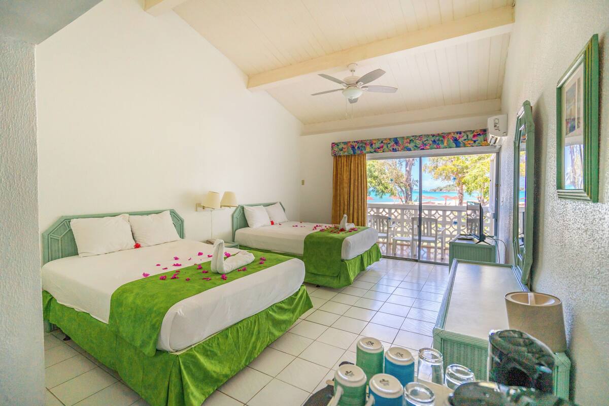 A hotel room with two beds, a balcony, and a view of the outside.