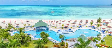 Un resort con una grande piscina, ombrelloni da spiaggia e vista sull'oceano.