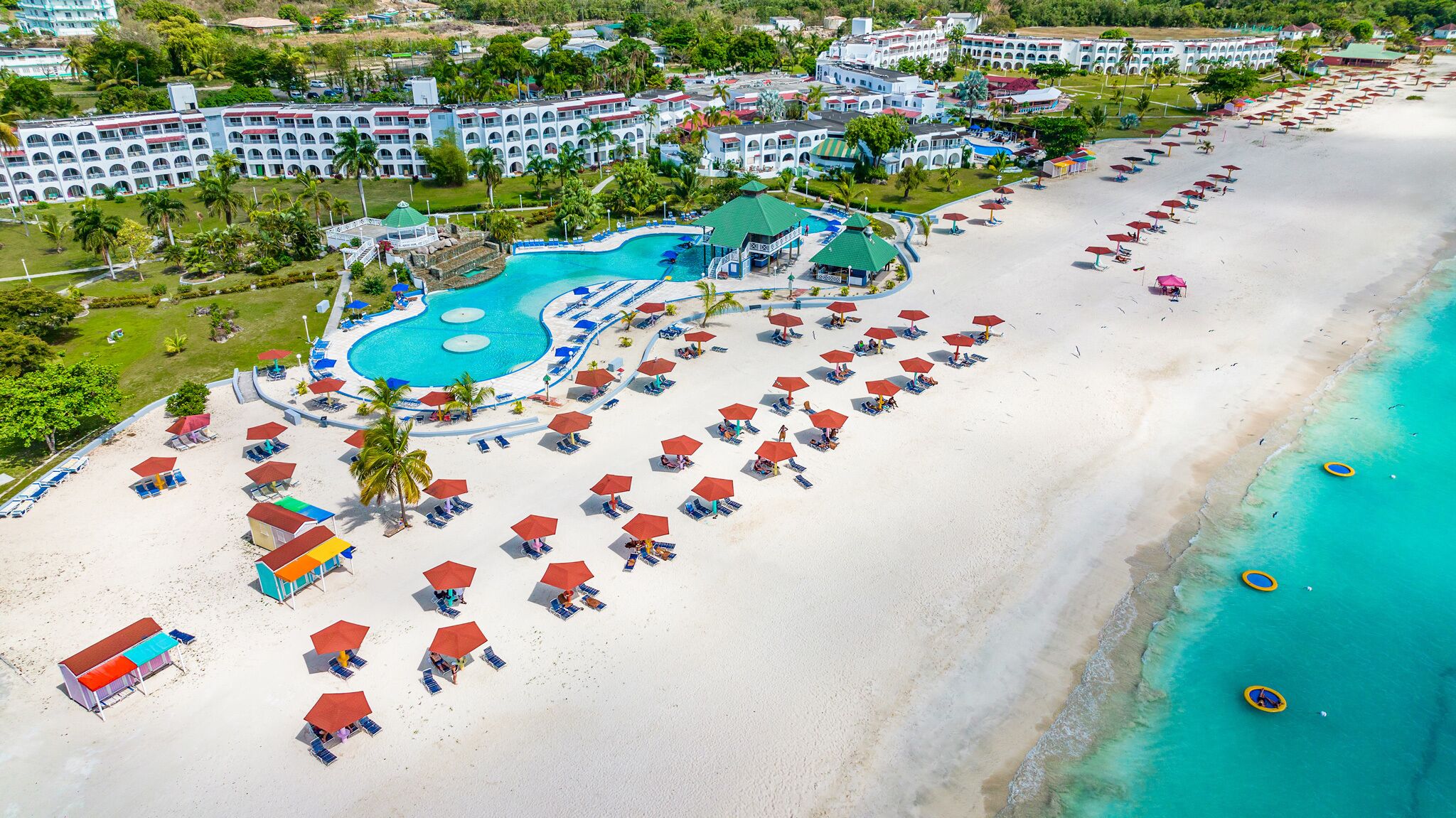 Ett semesterområde med en stor pool, en strand med parasoller och ett hotellkomplex.