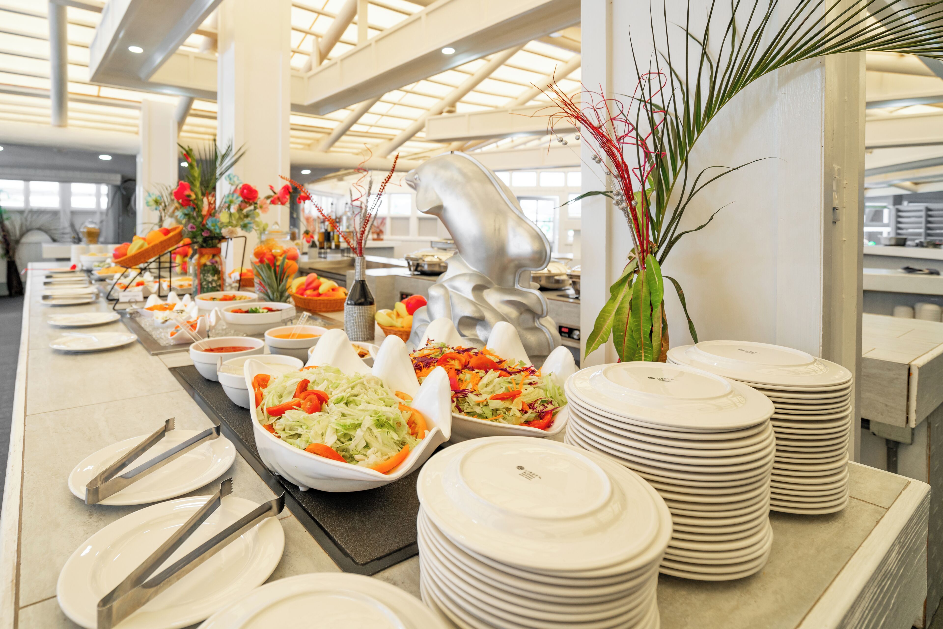 A buffet setup with various dishes, serving utensils, and decorative plants.