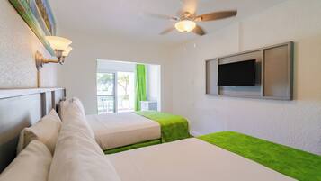 A hotel room with two beds, a ceiling fan, a TV mounted on the wall, and a window with green curtains.