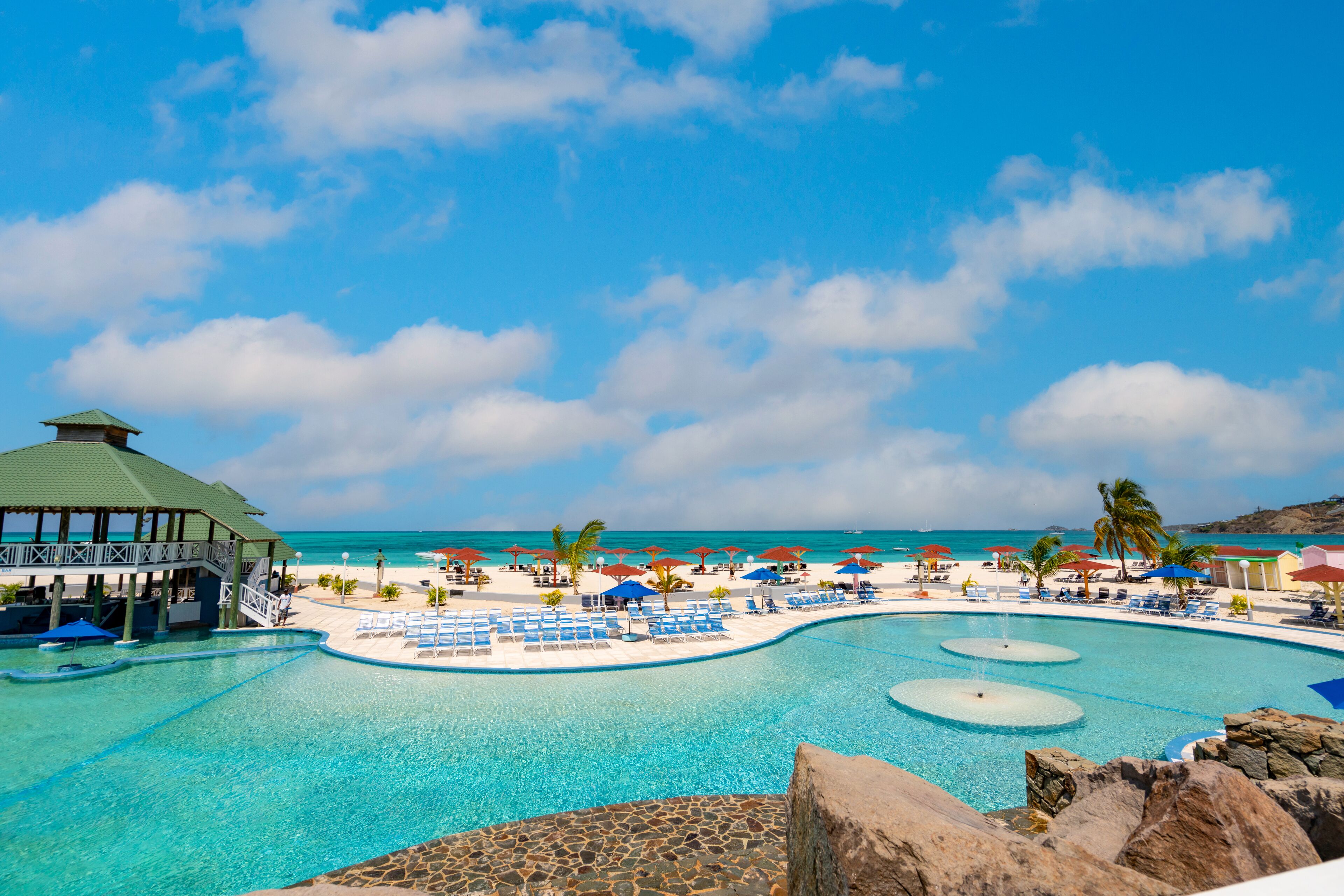 A resort pool with clear blue water, lounge chairs, umbrellas, and a view of the ocean.