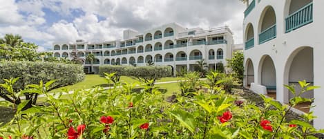 Un hotel de varios pisos con fachada blanca, varios balcones y un jardín con flores rojas.