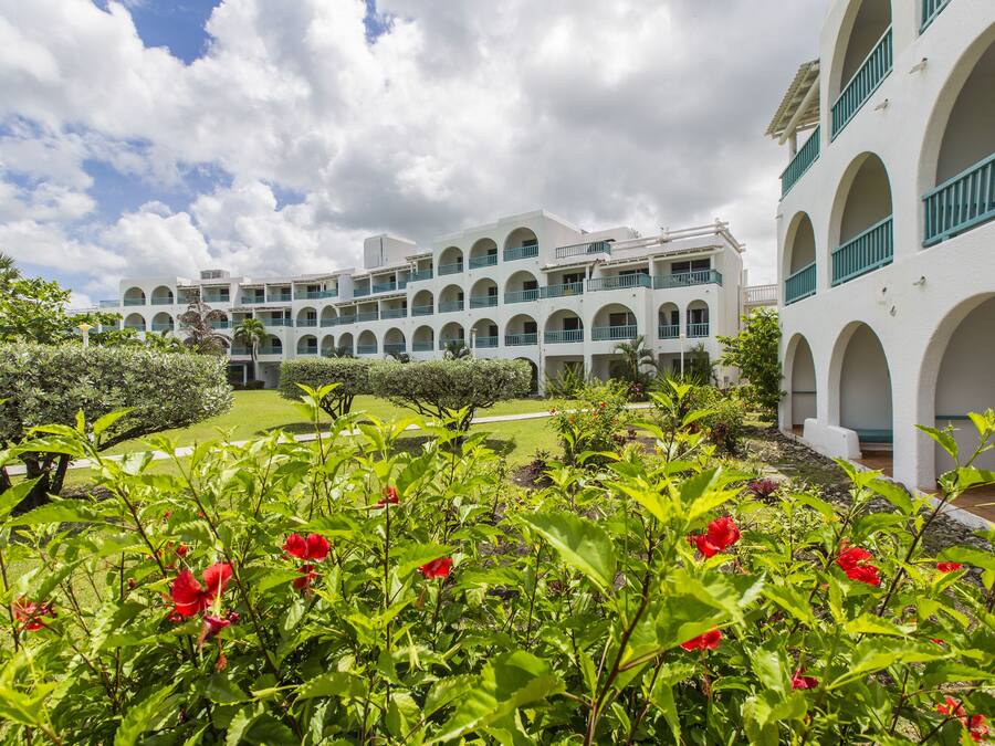 Un hotel a più piani con facciata bianca, numerosi balconi e un'area giardino con fiori rossi.