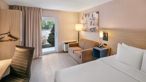 A hotel room with a bed, a desk, a chair, a sofa, a lamp, and a view of the outdoors.