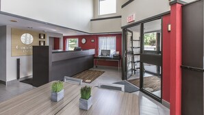 A hotel lobby with a reception desk, a clock, a computer, and a glass door leading outside.