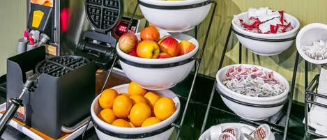 Un bufé de desayuno con diversas frutas, bocadillos y una máquina para hacer gofres.