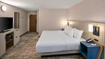 A hotel room with a bed, a TV, a desk with a lamp, and a door.