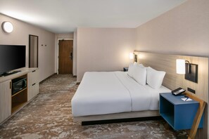 Une chambre d’hôtel avec un lit, une télévision, un bureau avec une lampe et une porte.