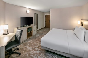 A hotel room with a bed, a desk with a chair, a television, and a mirror.