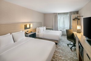 A hotel room with two beds, a desk with a TV, a chair, a bedside table with a lamp, and a window with curtains. - Comfort Inn Sydney - Cape Breton (Sydney)