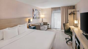 Habitación de hotel con una cama grande, un sofá, un escritorio con televisión y una ventana con cortinas.