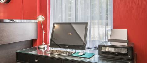 Un mostrador de recepción de hotel con un monitor Lenovo, una impresora Epson, una lámpara de escritorio y un reloj en la pared.