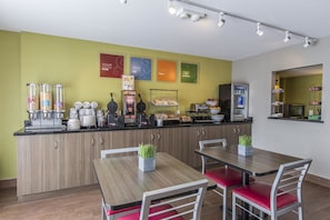 A modern kitchen area with a counter, various food items, and a seating area with tables and chairs.