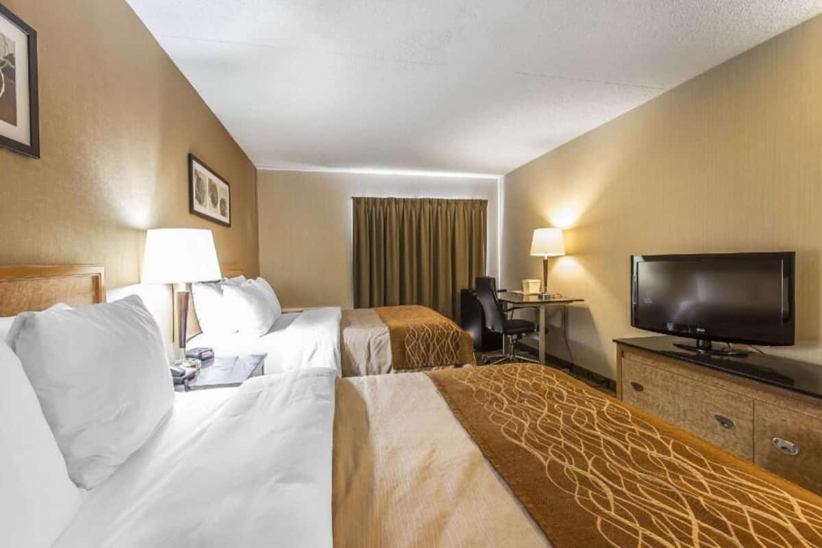 A hotel room with two beds, a desk, a television, and a chair.