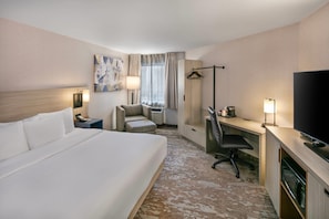 Une chambre d’hôtel équipée d’un lit, d’un bureau, d’une chaise, d’une télévision, d’une lampe et d’une œuvre d’art au mur.