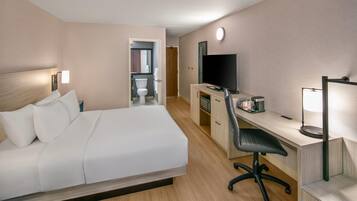 Ein Hotelzimmer mit Bett, Schreibtisch, Stuhl, Fernseher und einem durchgegangene Tür erkennbaren Badezimmer.
