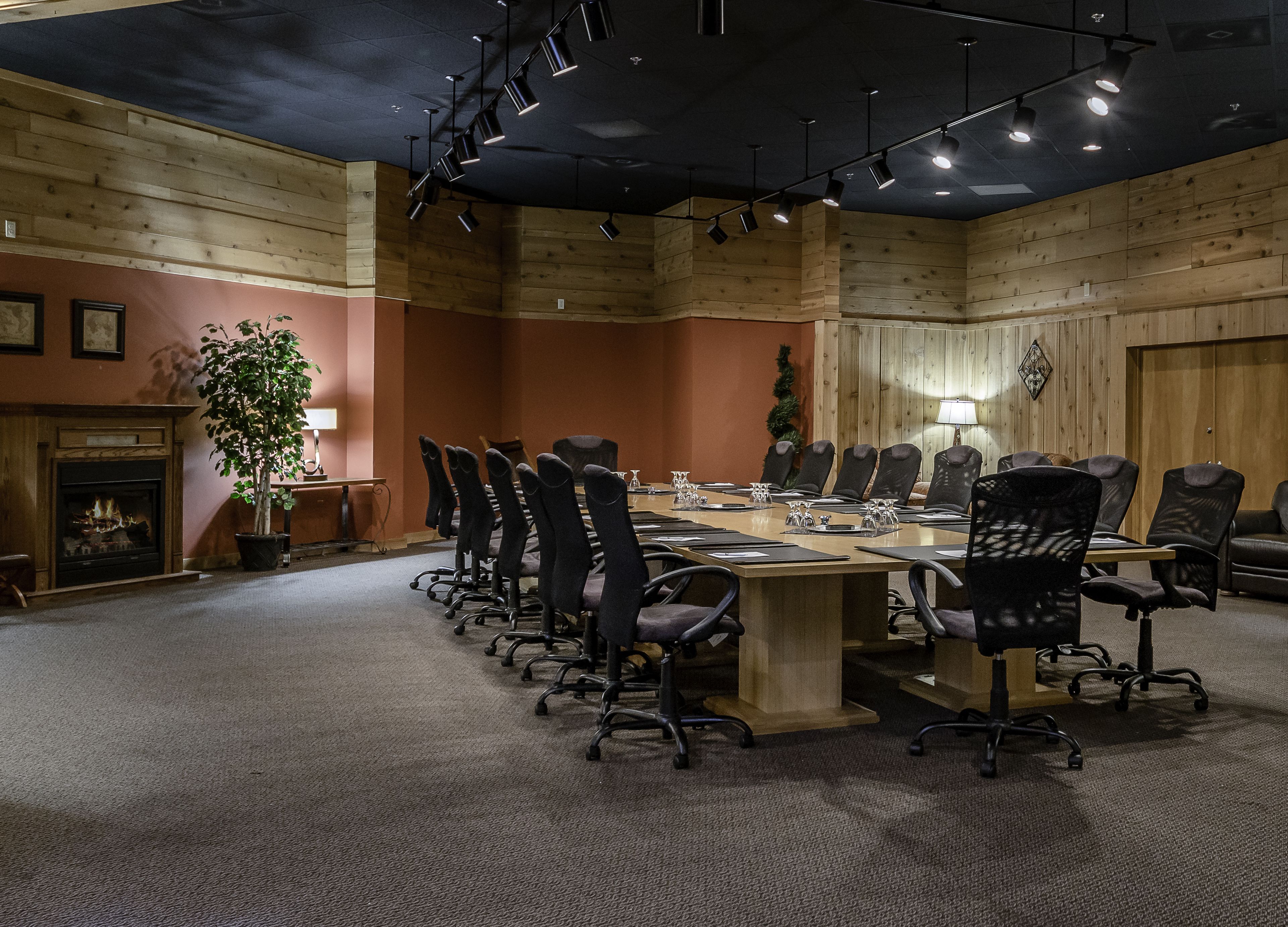 A conference room with a long table, multiple chairs, a fireplace, and wooden paneling.