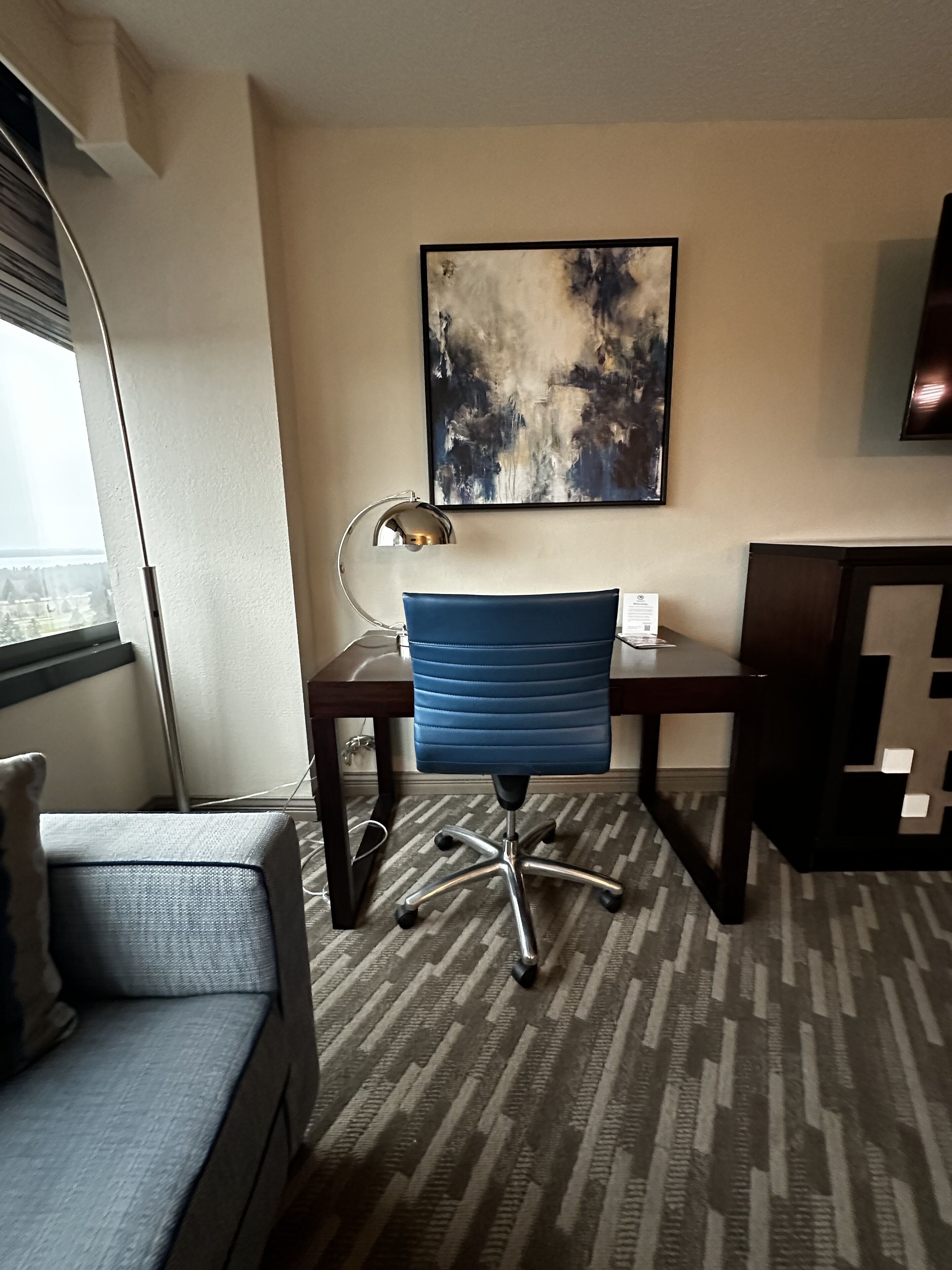 Ein Hotelzimmer mit Schreibtisch, Stuhl und einem großen, abstrakten Gemälde an der Wand.