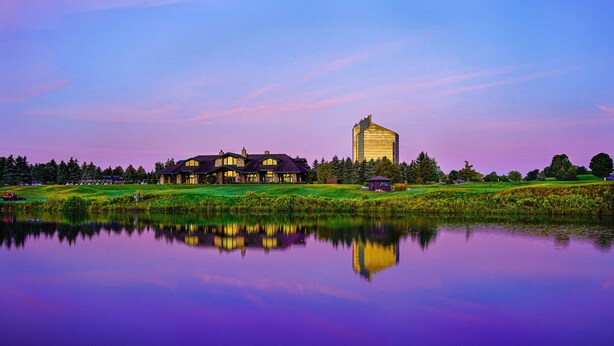 A large building with a modern design, surrounded by a well-maintained lawn and a calm lake reflecting the structure. - Grand Traverse Resort And Spa (Williamsburg)