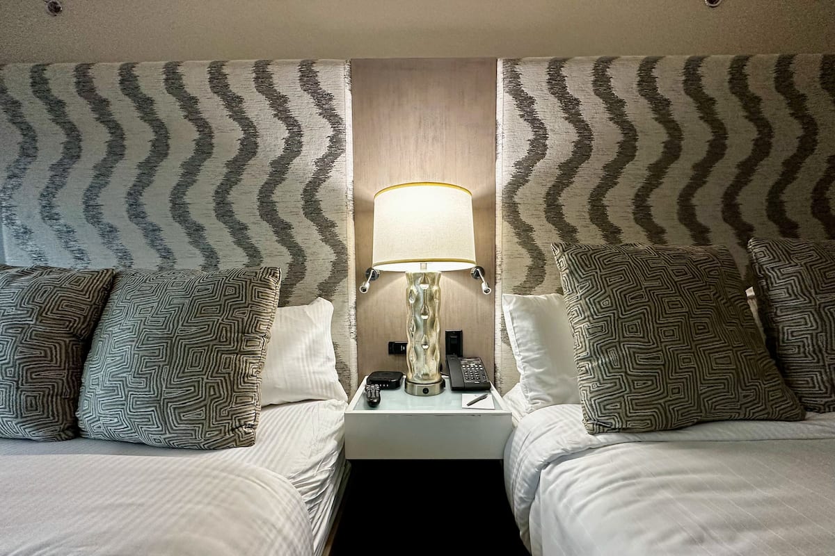 A hotel room with two beds, each with patterned pillows, a bedside lamp, and a telephone on the nightstand.