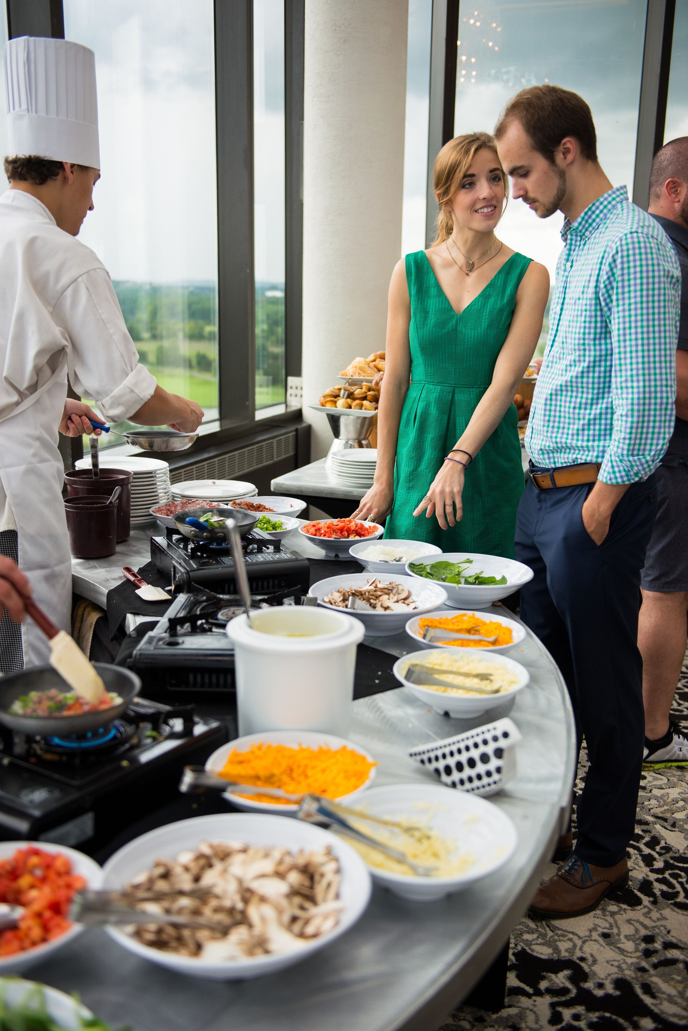 A buffet table with various dishes, a chef preparing food, and guests standing around.
