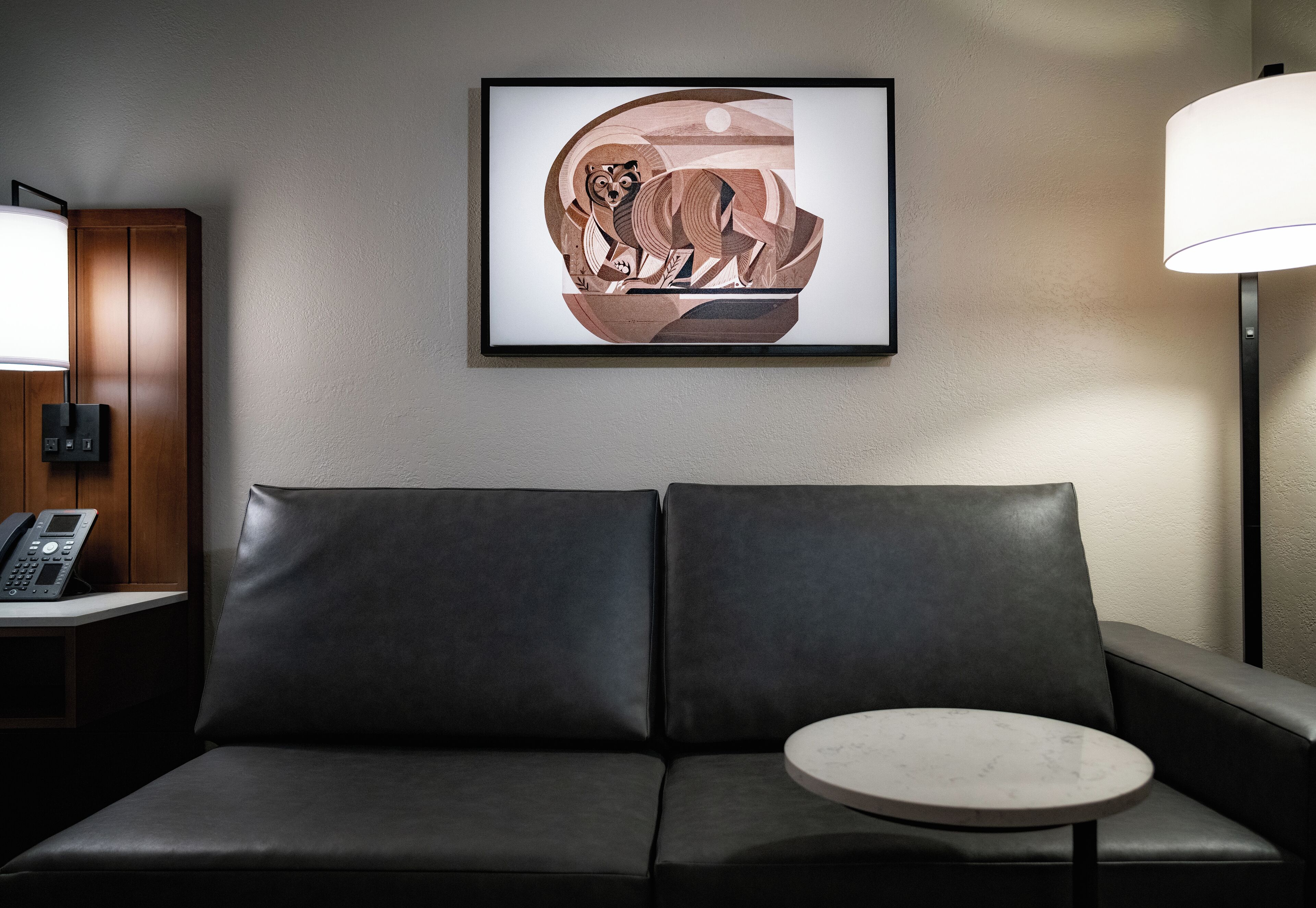Quarto de hotel moderno com um sofá de couro preto, uma mesinha redonda e uma obra de arte emoldurada na parede.