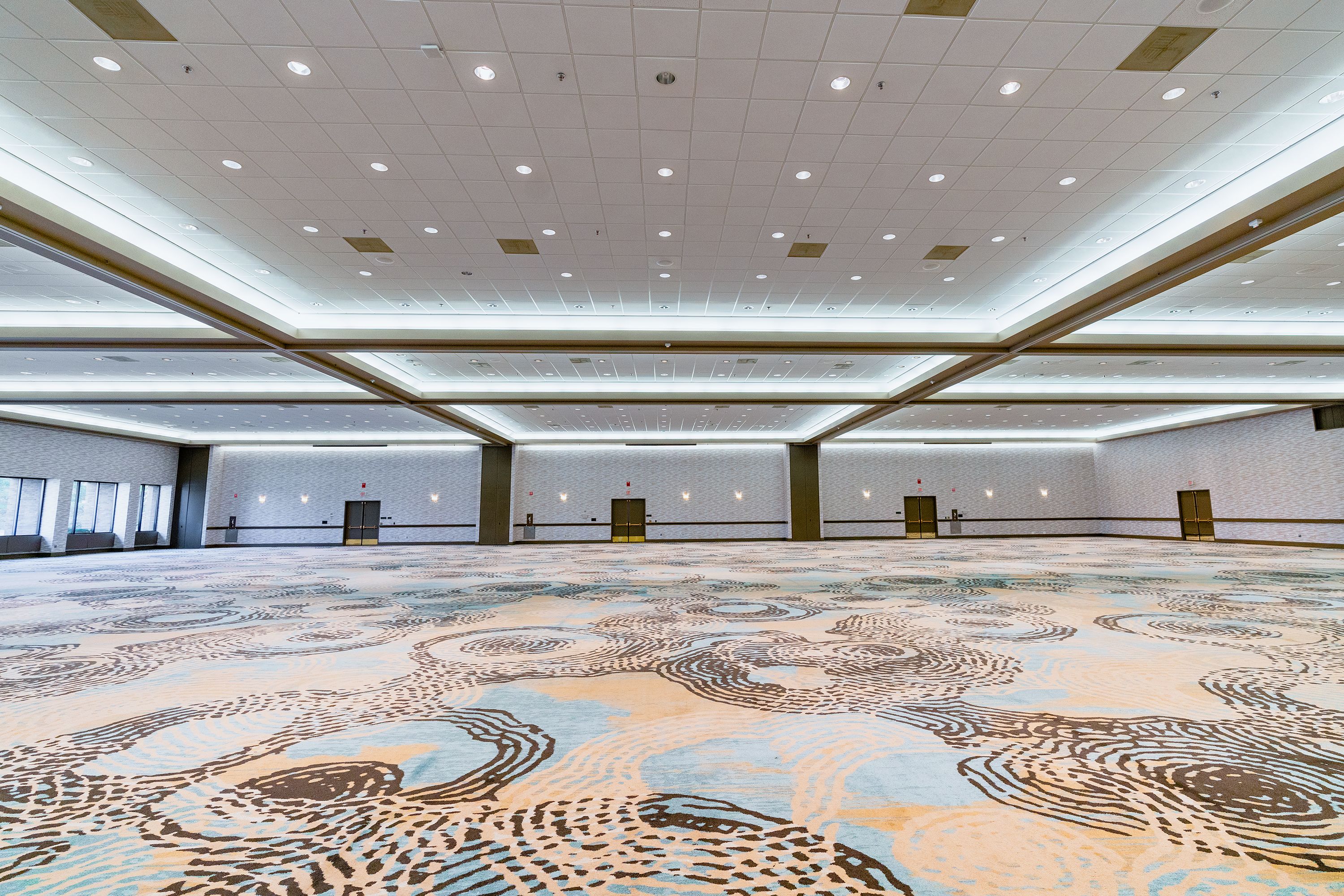 A spacious conference room with a patterned carpet, recessed lighting, and a high ceiling.