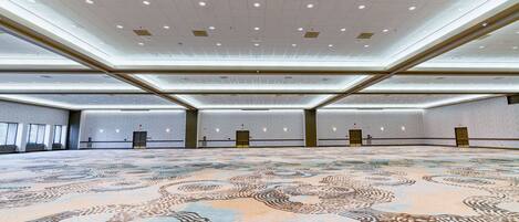 A spacious conference room with a patterned carpet, recessed lighting, and a high ceiling.