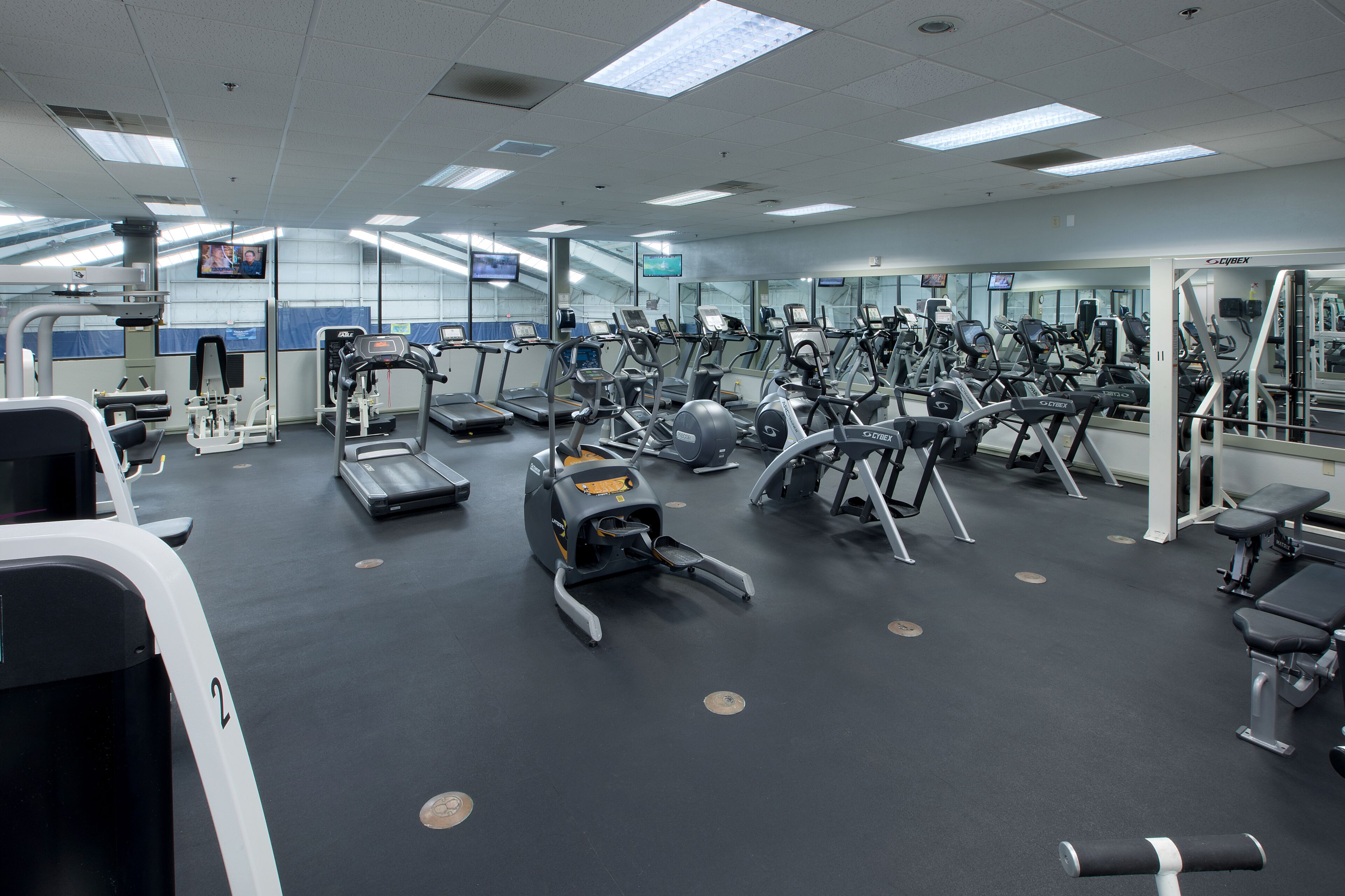 Une salle de sport équipée de divers appareils d’exercice, dotée de murs couverts de miroirs et de plusieurs écrans de télévision.