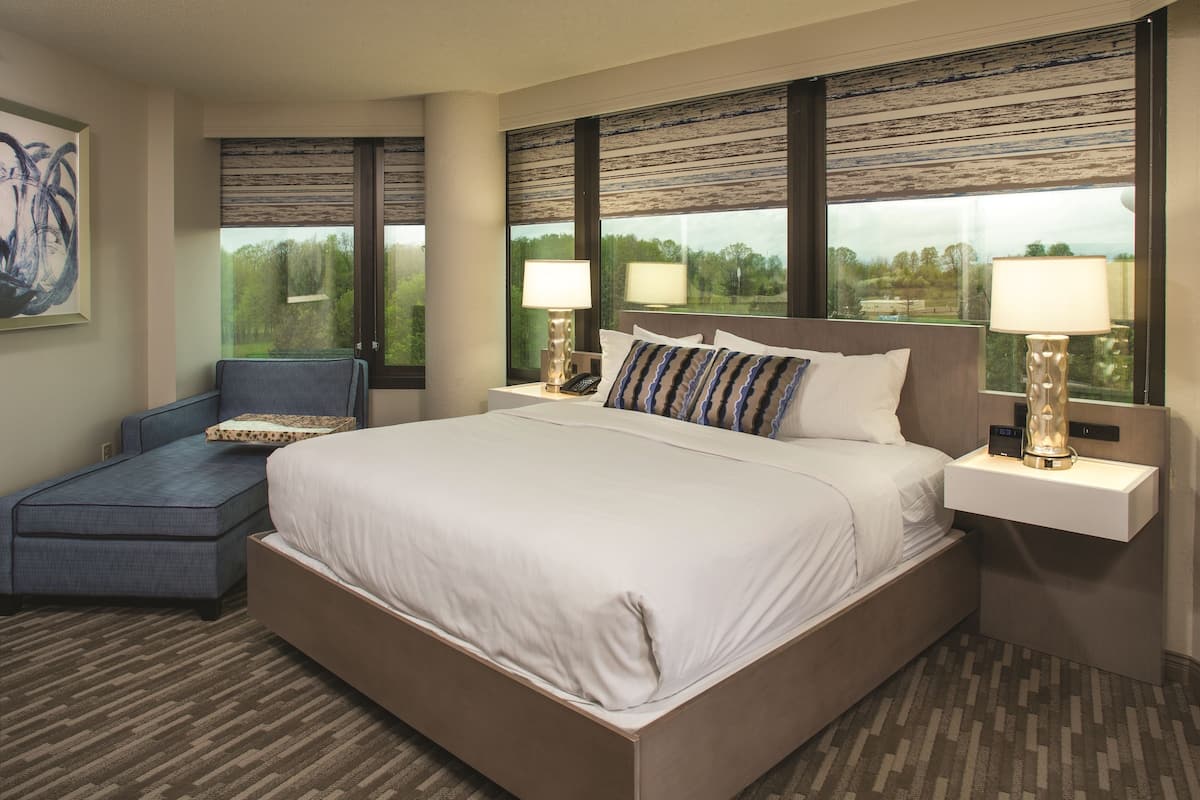 A hotel room with a large bed, a seating area, and a view of the outdoors.